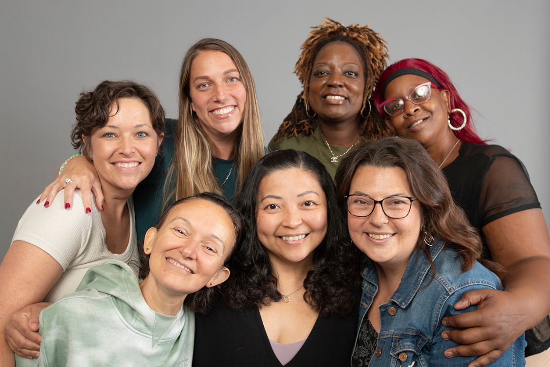 A group of diverse women, all who have metastatic breast cancer, hug and ham it up.