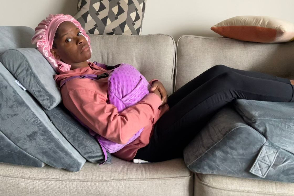 Nikki Taylor, back home from surgery, rests and recovers on her sofa, supported by bolster cushions.
