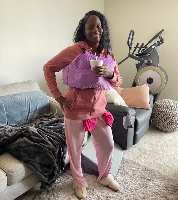 Nikki Taylor stands in her living room, recovering from breast surgery with a wearable cushion on her chest.