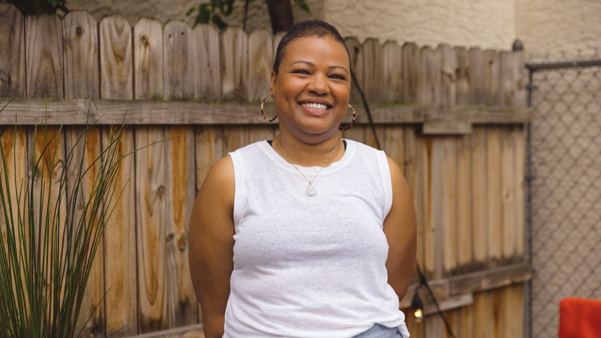 A Black woman smiling in front of a wooden fence