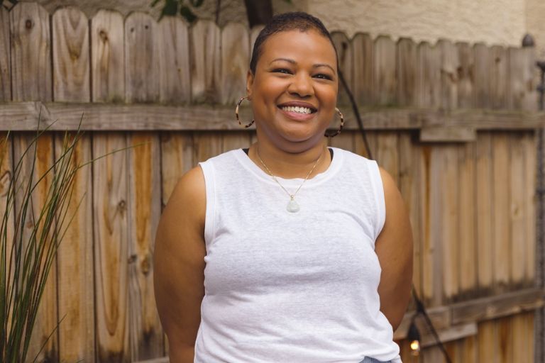 A Black woman smiling in front of a wooden fence