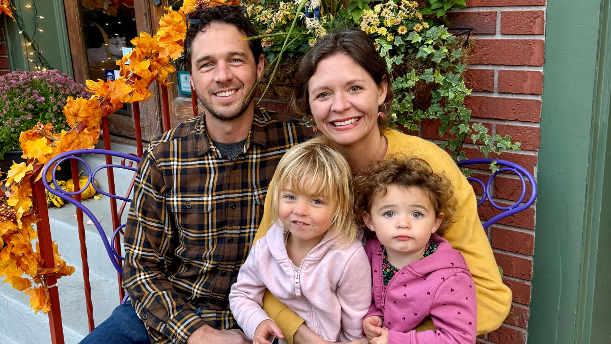 Kim Quick sits with her husband and two small children on their front steps, which are decorated with fall foliage.