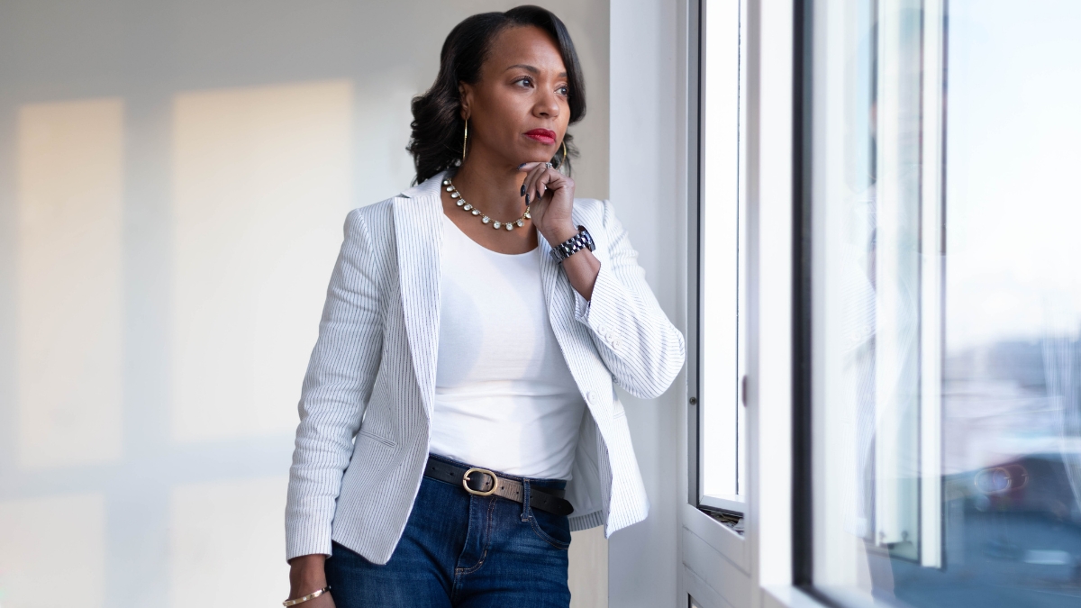 Concerned, a Black woman ponders an internal question as she looks out a window.
