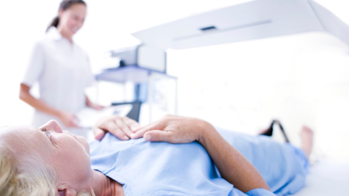 A woman undergoes a bone density scan with a nurse supervising.