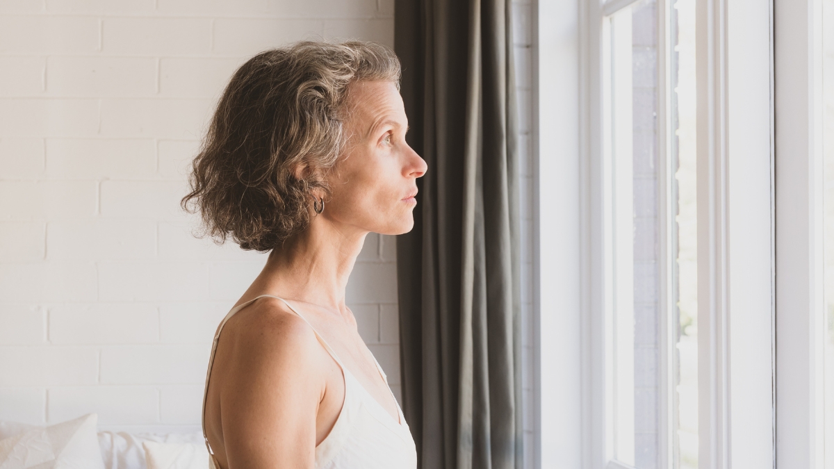 A mature white woman reflects as she looks out the window.