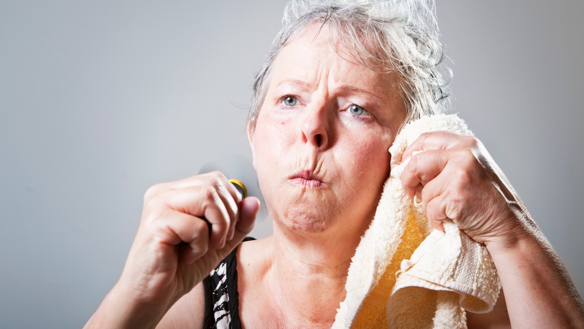 A mature white woman wipes the sweat from her face.