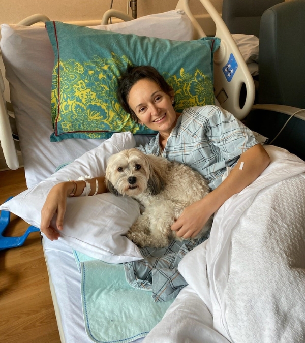 Florina Dragovic lies in a hospital with a confident smile, spooning her dog Peanut.