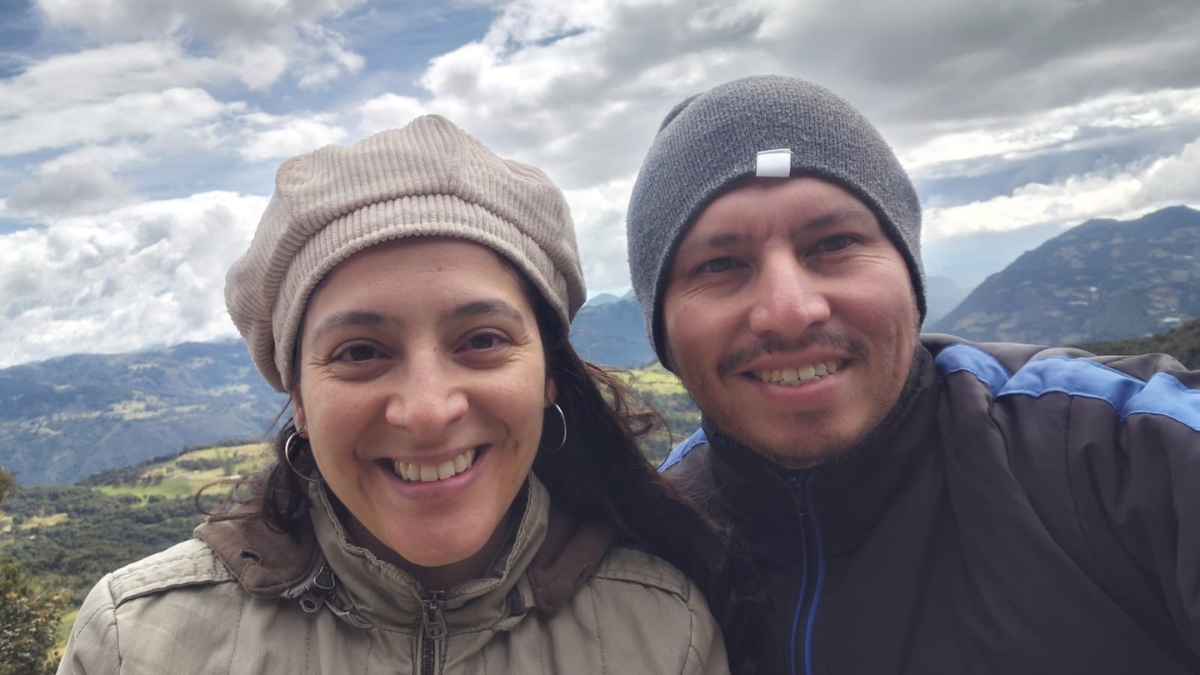 Gynna P. Quintero and her boyfriend Diego smile, mountain tops and big fluffy clouds behind them.