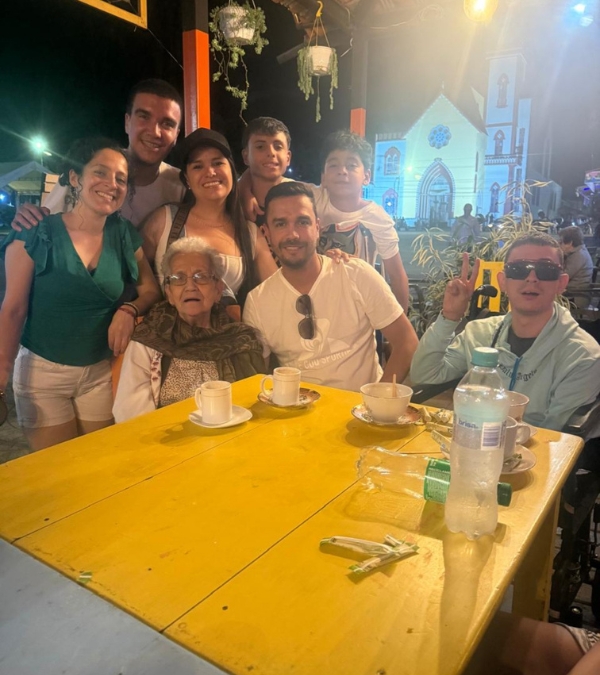 Gynna Quintero and family members are gathered at an outdoor table, a lovely church in the distance behind them.