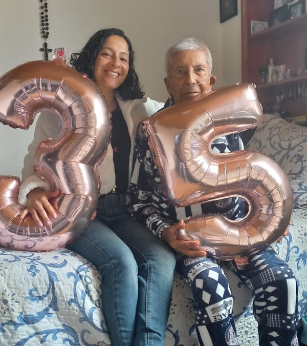 Gynna Quintero sits on the bed with her grandfather, holding up balloons for Gynna's birthday.