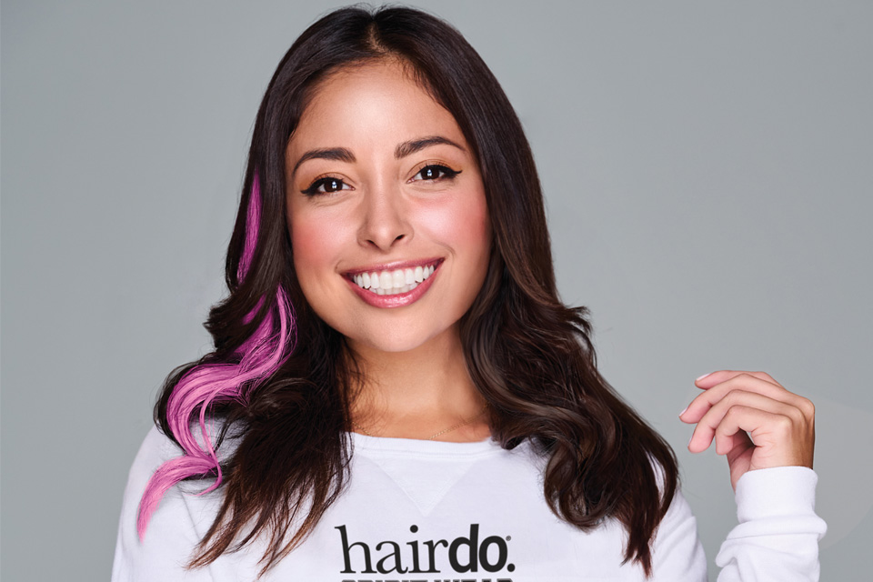A Latina woman smiling with a pink, way hair extension