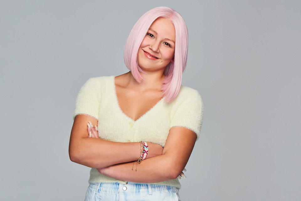 A white woman smiling, wearing a light pink bob wig