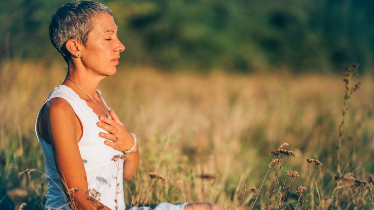 A woman is seated in a sunny field with a calm and peaceful facial expression.