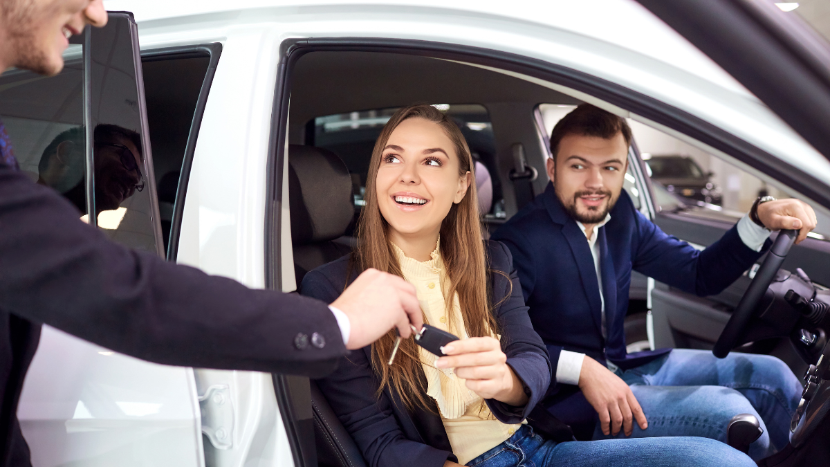 A car salesman handing over car keys to a couple sitting in a new car