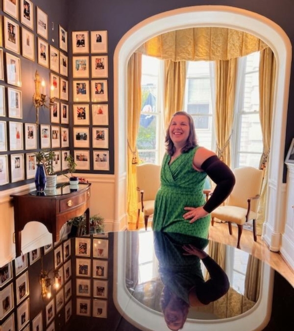 Framed by a formal, colonial style bay window, Meg Graves regards some framed and autographed pictures.