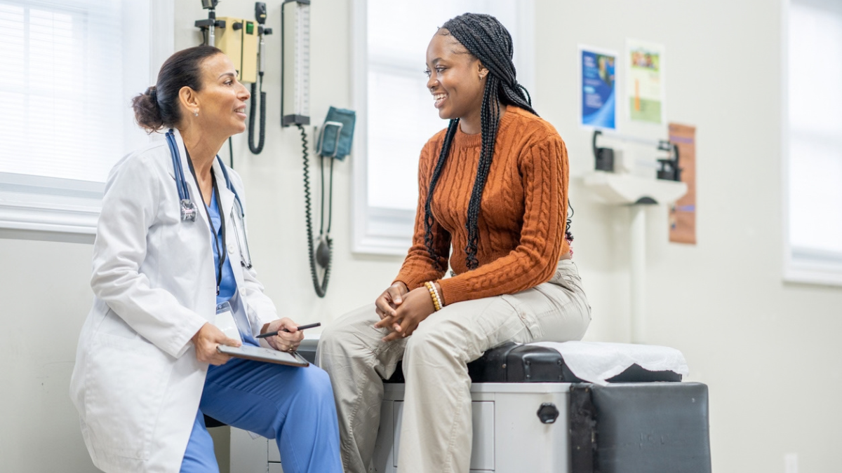 A white doctor talking to a Black patient in a doctor's office