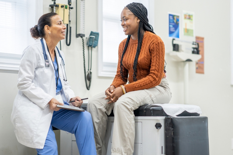 A white doctor talking to a Black patient in a doctor's office